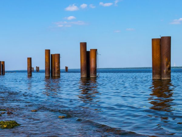 pexels-photo-8641002-8641002 Rusty steel poles protruding from ocean waters under a clear blue sky.